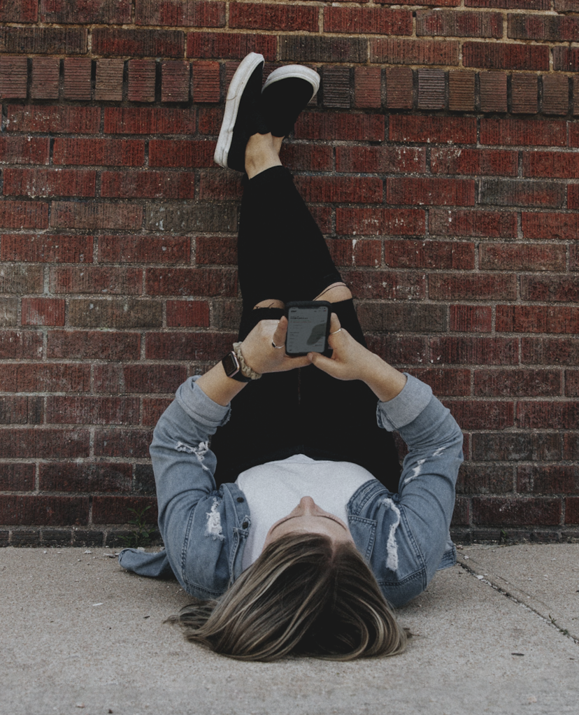 Woman laying down with feet rested against brick wall using the Stake app.