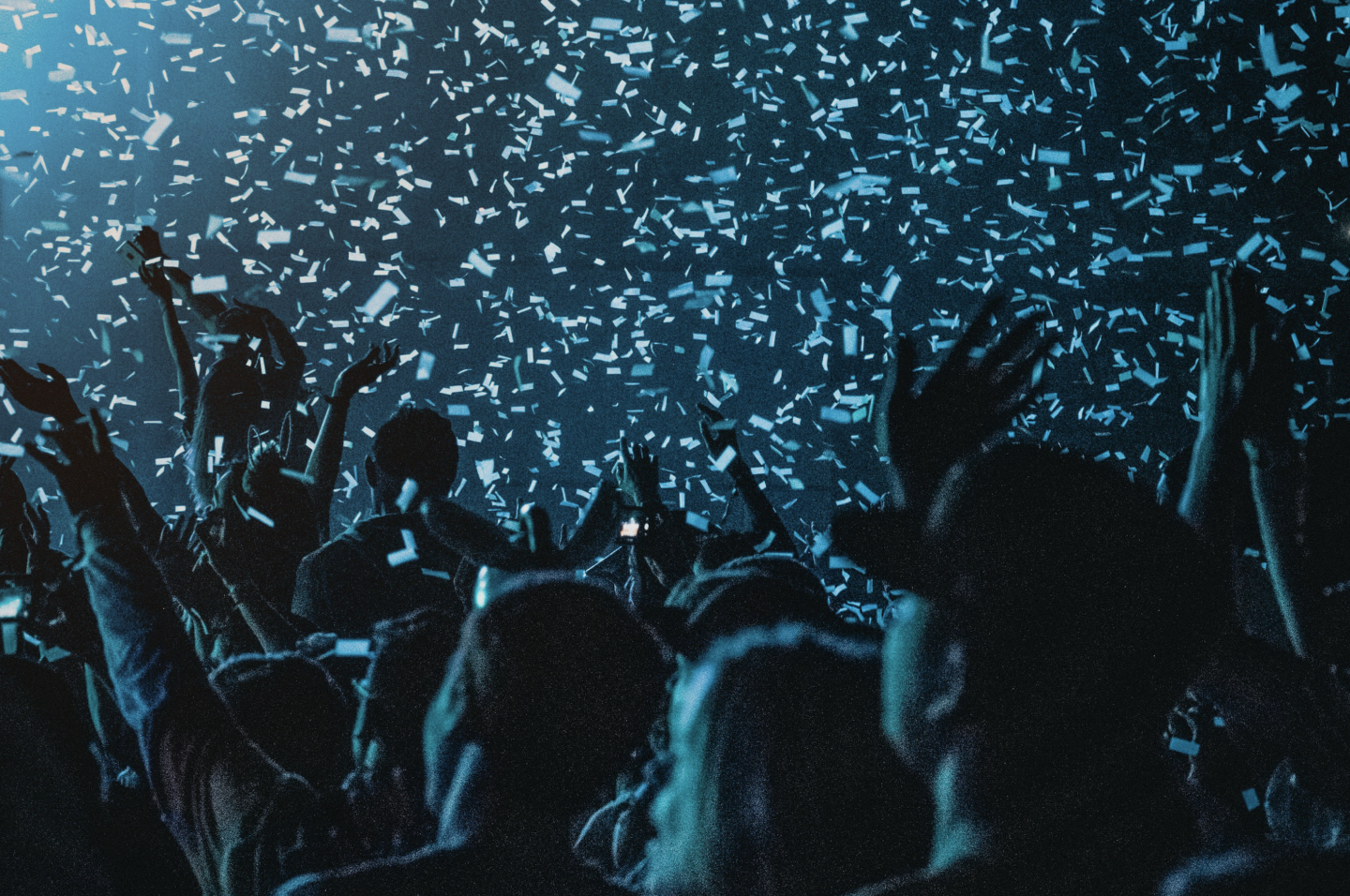 Paper confetti floating through the air onto an audience of dimly lit people watching a concert